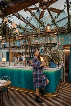 a woman standing in front of a bar with plants growing on the wall and ceiling