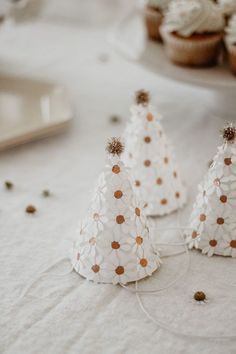 three small white christmas trees sitting on top of a table next to cupcakes