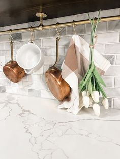 two copper mugs are hanging on the wall above a marble countertop with white tulips