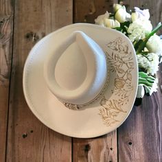 a white hat sitting on top of a wooden table next to flowers and a bouquet