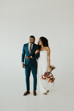 a man and woman standing next to each other in front of a white wall wearing blue suits