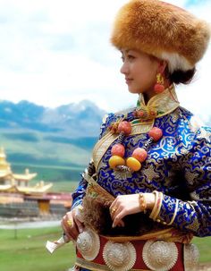 a woman dressed in traditional chinese clothing and fur headdress, with mountains in the background