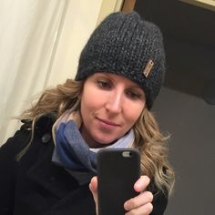 a woman is looking at her cell phone while wearing a hat and scarf in the mirror