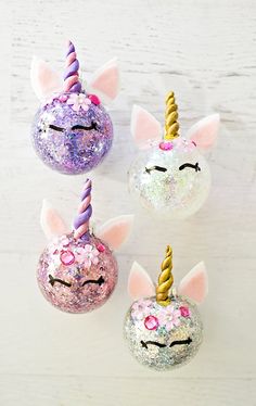 three unicorn ornaments are sitting on a white surface, one is pink and the other is purple