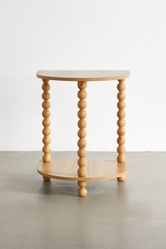 a round wooden table with three legs and two circular wood posts on the top, in front of a white wall