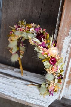 a wreath made out of dried flowers and feathers on a wooden bench in front of an old door