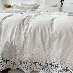 a bed with white sheets and lace on the bottom, in front of a window