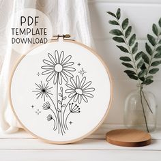 a cross stitch pattern with daisies on it and a potted plant in the background