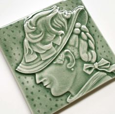 a green ceramic tile with a woman's face wearing a hat and bow tie