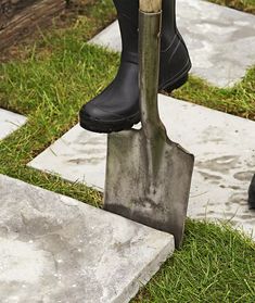 a pair of black boots and a shovel are on the grass near some stepping stones