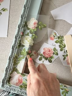 a hand is pointing at some flowers on the wall next to a mirror and papers