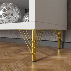 a white cabinet with gold legs and two silver balls in the back ground, on top of a wood floor