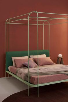 a green metal bed frame with pillows and blankets on it in front of an orange wall