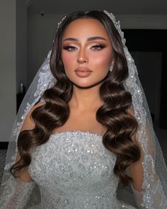 a woman in a wedding dress with long brown hair and veil on her head, posing for the camera