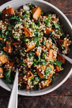 a bowl filled with rice and vegetables on top of a wooden table next to a spoon