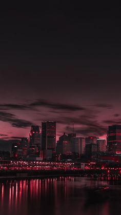 the city skyline is lit up at night with red lights in the foreground and dark clouds in the background