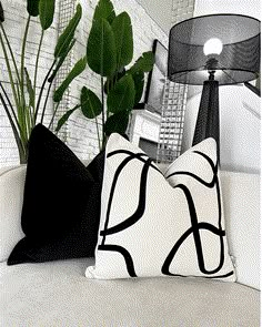 two black and white pillows sitting on top of a couch next to a green plant