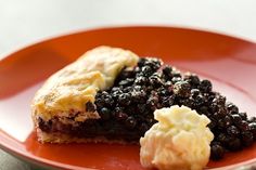 a piece of pie with blueberries and ice cream on it sitting on a red plate