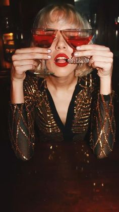 a woman holding up two glasses with red liquid in front of her face