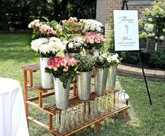 several vases filled with flowers sitting on a wooden stand in front of a sign