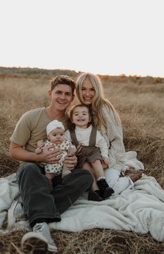 a man and woman sitting on top of a blanket holding a baby