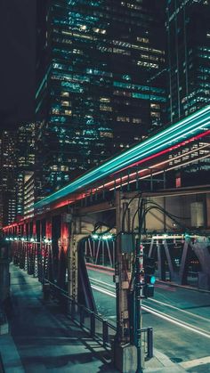 a city street at night with buildings lit up in the background and lights streaking across the road