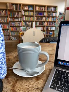 an open laptop computer sitting on top of a wooden table next to a coffee cup