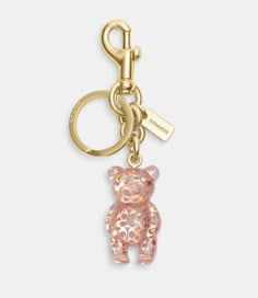 a pink teddy bear keychain hanging from a gold colored metal hook on a white background