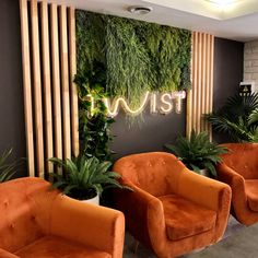 two orange chairs sitting next to each other in front of a wall with plants on it