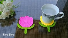 two crocheted flower coasters sitting on top of a table next to a coffee cup