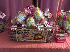 a basket filled with lots of toys sitting on top of a pink cloth covered table