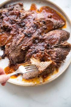 a person is holding a fork over some meat on a plate