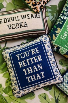 four embroidered pillows with words on them sitting on top of a green and white flowered surface