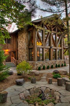 a stone and wood house with trees in the front yard, surrounded by large rocks