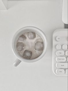 a coffee cup with ice cubes in it next to a remote control