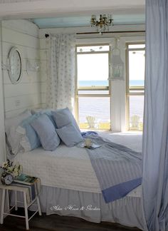 a white bed sitting next to a window in a bedroom under a blue and white curtain