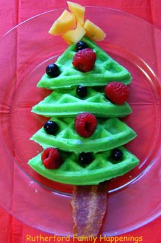 a christmas tree made out of waffles on a pink plate with strawberries and raspberries