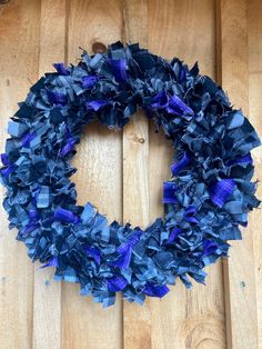 a blue wreath is hanging on a wooden door with purple and white ribbons around it