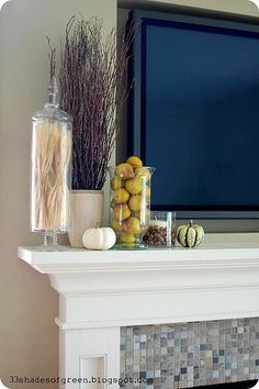 a white mantle with vases and fruit on it in front of a flat screen tv