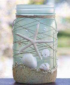 Decorative  beach themed sea green wide mouth mason jar  for table decor 12 quart 32 ounces  mason jars with wide mouth lid/band, hand painted in translucent sea green, coated at the base with sand and tiny glass pieces .It is decorated with natural polished hemp,  starfish shells ,beads ,sand dollar ,clam shells,to give it a coastal feel.   The inside of the jar is not painted. All mason jars come with a lid and band For best results keep it away from water and direct heat. To clean  gently wip Beach Themed Kitchen Table, Beach Themed Crafts Diy, Ocean Centerpiece Ideas, Sea Table Decorations, Sea Theme Decorations, Sea Decoration Ideas Ocean Themes, Beach Jars Diy Ideas, Beach Wedding Table Centerpieces My Wedding Favors, Beach Mason Jar Ideas