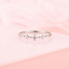 a white gold ring with three diamonds on it, sitting on a pink cloth background