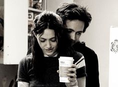 black and white photograph of two people looking at something on a cell phone while holding a coffee cup