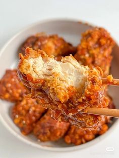 a white bowl filled with meat covered in marinara sauce and topped with chopsticks