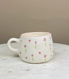 a white cup with pink flowers and hearts painted on the inside is sitting on a marble table