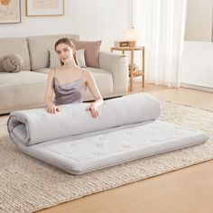 a woman sitting on top of a mattress in a living room next to a couch