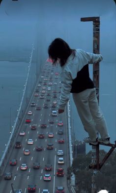 a person on a skateboard is standing on the edge of a high bridge with cars going over it