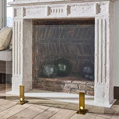 an old fireplace with gold candles and vases on the mantle