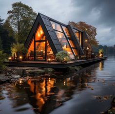 a house on the water is lit up at night with lights in it's windows