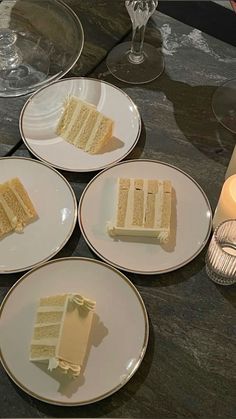 four plates with slices of cake on them sitting on a table next to wine glasses