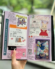 a hand holding an open book with pictures and stickers on the pages in it